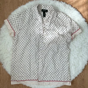 Prickig silkesblus från Ralph Lauren - Snygg kortärmad skjorta i 100% silke från Ralph Lauren. Perfekt för dig som gillar en retrovibe och mjuka material. Storlek L(40) men passar även M(38).