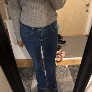 Blå bootcut jeans med vita sömmar - Snygga blå jeans med bootcut passform och markerade vita sömmar. Klassisk femficksmodell med knappstängning bak på fickan och låg midja. Jeansen har en cool, lite retro look och är gjorda i jeansmaterial med stretch för extra komfort.