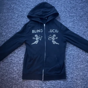 Svart hoodie med strass från Blinglucid - Svart hoodie från Blinglucid! Ett fåtal pärlor från texten har lossnat vilket såklart spelar roll vid prissättningen!✅💸 Förutom pärlorna så är allt som det ska vara!