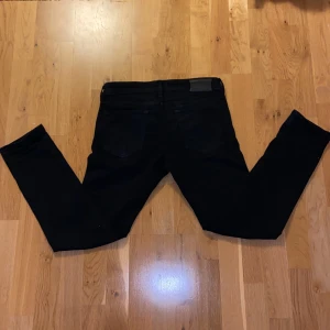 Svarta Slim Glenn jeans från Jack & Jones & Jones - Svarta jeans från Jack & Jones, modell Slim Glenn. Snygg slim fit som passar bra för dig som gillar lite mer tajtare jeans med steretchig material. Ett år perfekt vardags jeans som går hem i alla typer av tillfällen. 