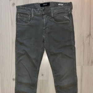 Replay Anbass grå/gröna jeans slim fit - Snygga grå jeans från Replay, modell Anbass. Slim fit med klassisk femficksdesign och diskreta Replay-detaljer på fickan. Perfekt passform och stilren look som funkar till sneakers eller boots.