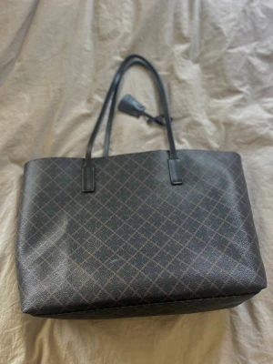 Svart shoppingväska med rutigt mönster - Väska ”Abigail” från Marlene Birger i färgen dark chocolate. Väskan är rymlig och passar bra till både vardag och jobb. Det finns slitage och en liten färgfläck på både framsida och baksida, se bilder för mer detaljer. 