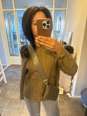 Grå axelväska med croco-mönster från cw<3 - Snygg grå axelväska med croco-präglat mönster och bred justerbar rem. Väskan har en stilren, rektangulär form och är tillverkad i skinnimitation. Metallspänne på remmen för enkel justering❤️ord pris 499kr