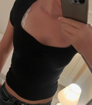 Svart croppad topp från Gina Tricot - Svart topp från Gina Tricot i croppad modell med korta ärmar och snygg v-ringad hals. Toppen har en liten rynkning framtill som ger extra stilpoäng. Mjuk och stretchig bomull som sitter skönt och framhäver figuren. Perfekt till jeans eller kjol.