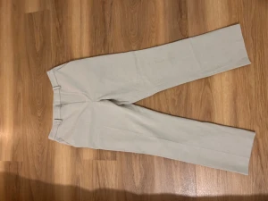 Beige byxor från Uniqlo M - Snygga beige byxor från Uniqlo i storlek M med rak passform och klassiska fickor bak. Materialet är en mix av polyester, viskos och elastan som ger en mjuk och bekväm känsla. Perfekt för dig som gillar stilrena och enkla byxor.