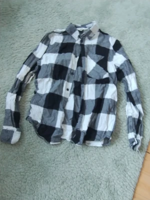 Rutig skjorta från H&M i svart och vitt - Snygg rutig skjorta från H&M i storlek 158. Skjortan har stora svartvita rutor, klassisk krage och knappar framtill. Tillverkad i mjuk bomull och har långa ärmar med knapp vid manschetten.Sparsamt använd 