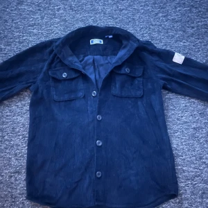 Mörkblå manchester overshirt Jack & Jones - Tvärfet jack and jones skjorta/overshirt! Manchester tyg vilket gör att den är bekväm samtidigt som den är stilren🍾Märket som ses på bild 3 sitter på vänster arm och bidrar med detalj!✅