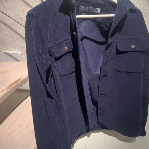 Mörkblå manchester overshirt Polo - Snygg mörkblå overshirt från Polo Ralph Lauren i klassisk passform. Tillverkad i mjuk manchester med två bröstfickor med knappstängning och stilrena detaljer. Perfekt att slänga över en t-shirt för en chill look.