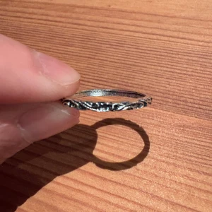 Tunn silverring med snirkligt mönster - Säljer en tunn och stilren ring i silverfärgat metall med snirkligt, detaljerat mönster runt hela ringen. Perfekt för dig som gillar diskreta men unika accessoarer. Ringen är lätt och passar både som ensam detalj eller i kombination med andra ringar.