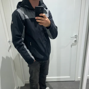 Svart och grå skidjacka Five Seasons - Mycket snygg svart och grå skidjacka/vinterjacka från Five Seasons med avtagbar huva och flera dragkedjeförsedda fickor. Jackan har en sportig look med kontrastpaneler och justerbar huva. Perfekt för dig som gillar stilren och funktionell design. Kan skickas!