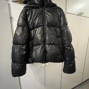 Svart pufferjacka från H&M med huva - Säljer en svart pufferjacka från H&M i storlek S. Jackan har en oversized look, huva och dragkedja framtill. Perfekt för kalla dagar med sin fluffiga och quiltade design. Enkel och stilren modell som passar till det mesta.