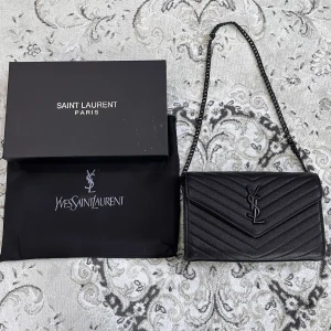 Svart quiltad axelväska Saint Laurent - PRIS GÅR ATT DISKUTERAS. Snygg svart axelväska från Saint Laurent med klassisk YSL-logga framtill. Väskan har ett quiltat mönster och en stilren kedjerem i svart metall. Perfekt storlek för det viktigaste och tillverkad i exklusivt skinn.