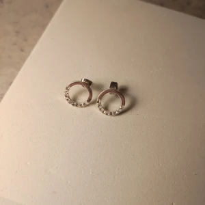 Silverörhängen med cirklar och stenar - Snygga örhängen i silverfärgad metall med öppen cirkelform och små gnistrande stenar längs nederkanten. Perfekta för dig som gillar stilrena smycken med lite extra bling. Stiftmodell som sitter bekvämt på örat.