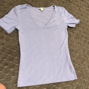 Ljuslila v-ringad t-shirt från Gina Tricot - Säljer en stilren ljuslila t-shirt från Gina Tricot med v-ringad hals och korta ärmar. T-shirten är gjord i mjuk bomull och har en slim passform som sitter snyggt. 