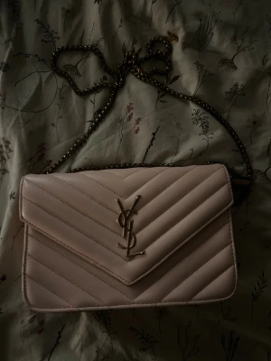 Ljusrosa YSL axelväska med kedja - Säljer en ljusrosa axelväska från YSL med guldfärgad kedja. Fick den i julklapp för ett par år sen och har knappt använt den, väldigt bra utrymme och fin. 