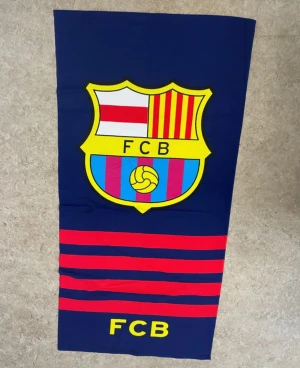 FC Barcelona väst med klubbmärke - Snygg väst i mörkblått med FC Barcelonas ikoniska klubbmärke framtill. Västen har röda och blå ränder samt gula detaljer och texten FCB. Perfekt för dig som älskar fotboll och vill visa ditt stöd för Barca. Materialet är mjukt och lätt bomull.