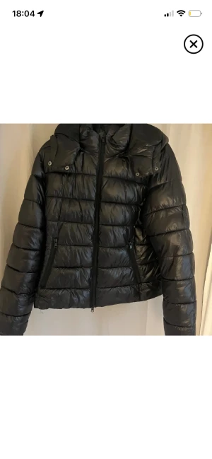 Svart pufferjacka med huva - Säljer en svart pufferjacka i bra skick! Det har en liten lagning på ena armen men syns ingenting! Pris kan diskuteras! Liten i storleken så passar M/S men är i L