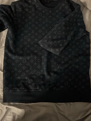 Svart Louis Vuitton sweatshirt M - Marinblå sweatshirt från Louis Vuitton i storlek M men den passa folk som har storlek S, med ikoniskt monogrammönster över hela tröjan. Rund halsringning och ribbade muddar vid ärmslut och nederkant. Tillverkad i Frankrike, riktigt lyxig vibe och perfekt för dig som gillar designer.