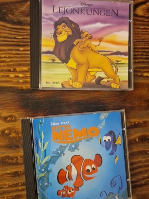 Lejonkungen & Hitta Nemo (Disney Klubben ljudbok/CD) - Två klassiska Disney-berättelser på CD: Lejonkungen och Hitta Nemo. Perfekt för dig som älskar äventyr, vänskap och ikoniska karaktärer. Lyssna på spännande historier med Simba, Nemo och deras vänner. Passar både unga och unga vuxna som vill återuppleva magiska Disney-stunder. Fodralet till lejonkungen är skadat så det håller inte ihop när man öppnar (se bild). Det finns även mindre repor på CD-skivorna men inget som störde när de användes senast. Kunde dock inte provspela dem nu.