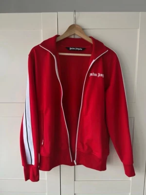 Palm Angels tröja  - Säljer en röd palm angels kofta väldigt fräsch, fläckfri och inga skador 9/10 skick storlek M äkta såklart, använd ett par fåtal gånger väl omhändertagen kan mötas i Västerås kan även frakta runt om hela Svergie, tveka inte och hörs av dig vid frågor priset är då inte hugget i stenet! 