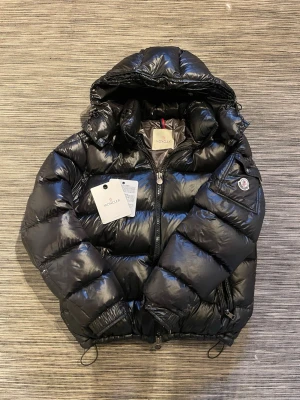 Svart Moncler Maya pufferjacka - Säljer en stilren och äkta moncler maya! Tyvärr så kan man bara lägga in max 7 bilder men om ni är intresserade så skriv till mig så har jag ungefär 10 bilder till där man se alla detaljer på jackan! (Tags, sömmar osv) Nfc-scan funkar både vid qr-koden och på armen. Man kan spänna både luvan och midjan så att den passar vem som helst! Storlek 3 (M). Jackans nypris är runt 19500kr. Man kommer till den exakta jackan på monclers hemsida vid Nfc-scannen på armen. Som sagt skriv om ni är intresserade
