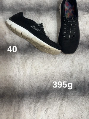 Svarta Skechers sneakers strl 40 - Svarta Skechers sneakers med vit sula och elastisk snörning. Ovandelen är i mesh-liknande syntetmaterial och innersulan har färgglatt mönster. Skorna har rund tå och platt sula, perfekta för dig som gillar bekväma och lätta skor.🌸 Lite skav längst fram och sidan av sulan har vikt sig lite på sidan ( känns inte och går att lägga rätt)  Ej tvättade. Storlek 40