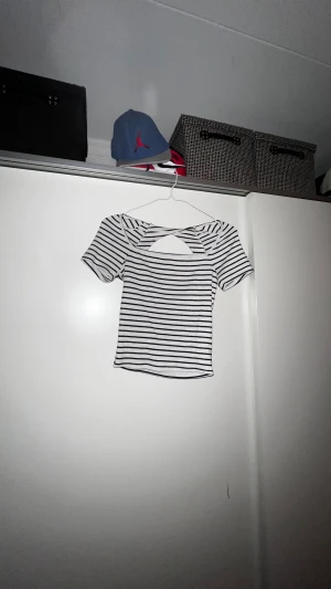 Randig croppad topp med öppen rygg - Säljer en vit och svart randig croppad topp från Gina tricot med korta ärmar och snygg öppen rygg med twistad detalj. Toppen är ribbad och har en tight passform. Använd ett fåtal gånger 😊💞💞