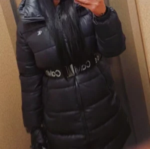Svart pufferjacka från Calvin Klein - Säljer en svart pufferjacka från Calvin Klein med markerat bälte i midjan och hög krage. Jackan har lång ärm och dragkedja framtill. Perfekt för kalla dagar och har en snygg, modern look med logga på bältet.