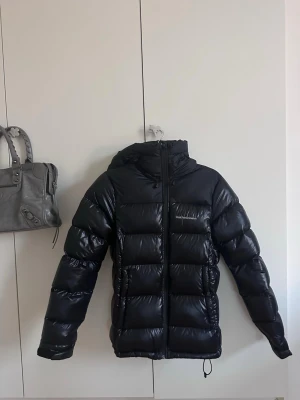 Svart pufferjacka Peak Performance XS - Säljer en svart pufferjacka från Peak Performance i storlek XS. Nypris är 3990kr. Jackan har en glansig finish, huva med dragsko och dragkedja framtill. Klassisk quiltad look och diskret logga på bröstet. Perfekt för kalla dagar när du vill vara både varm och snygg.
