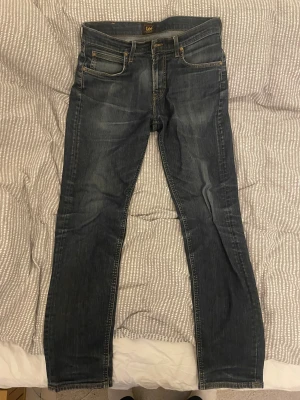 Lee jeans - Säljer ett par blå slim jeans från Lee. Jeansen är smått slitna och har en archive stil. Modellen är Arvin, storlek 30:32. Använda under en säsong men inga defekter tillkommer.