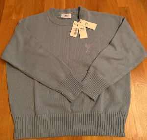 Ljusblå stickad tröja från Ami - Snygg ljusblå stickad tröja från Ami Alexandre Mattiussi med ribbade muddar och rund hals. Tröjan är oversized och passar den som är M/L eller större. 