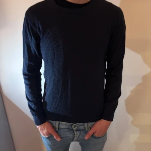 Mörkblå stickad tröja J.Lindeberg - Snygg mörkblå stickad tröja från J.Lindeberg i storlek M. Tröjan har en rund halsringning och ett diskret strukturerat mönster i materialet. Perfekt för lager-på-lager.                               Pris kan diskuteras!