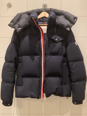 Moncler jacka - M/L - Säljer min Moncler Brazeau Giubbotto, en ovanlig och mycket eftertraktad modell som sällan dyker upp på andrahandsmarknaden. Jackan är otroligt stilig med sin kortare och karakteristiska Moncler-detaljer. Modellen är tillverkad i en exklusiv ullmix som ger ett lyxigt uttryck och samtidigt håller värmen riktigt bra. Perfekt för både vardag och mer uppklädda tillfällen. Skick: Bra (bilder finns på slitskador) • Modell: Moncler Brazeau Giubbotto • M/L (size 4) 