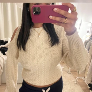 Beige stickad tröja med coldshoulder - Säljer en beige stickad tröja med snygg kabelstickning och offshoulder-detalj. Tröjan är croppad och har långa ärmar med bred mudd. Perfekt för dig som vill ha en trendig och mysig look.