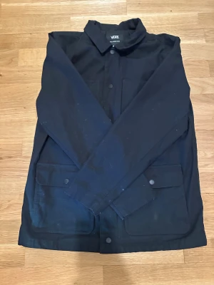 Svart Vans Drill Chore Coat - Hej jag säljer en Svart Vans Drill Chore Coat. Den har långa armar och passar Street och Grish stilen bra. Den kostar nu 800-900 ny