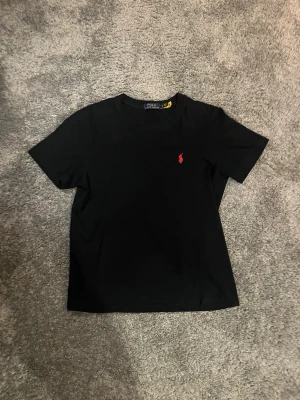 Svart t-shirt från Polo Ralph Lauren - Svart t-shirt från Polo Ralph Lauren i mjuk bomull. Den är i väldigt fint skick och andvänt max 10 gånger. Storlek S och passar dig som är ca 170-180 