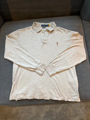Polo Ralph Lauren långärmad pikétröja, Medium, Fint skick - Snygg beige långärmad pikétröja från Polo Ralph Lauren i klassisk passform. Tröjan har krage, tre knappar framtill och den ikoniska broderade polospelaren på bröstet. Mjuk bomullskvalitet som är skön mot huden och passar perfekt till jeans eller chinos. Priset är förhandlingsbart. Skriv till mig om ni vill ha mer bilder! Jag svarar er snabbt. Passformen är Classic Fit