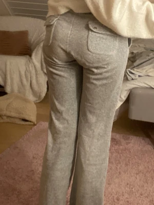 Gråa juicy couture del rey byxor - Säljer ett par grå mjukisbyxor med raka ben och bred resår i midjan. Byxorna har stora fickor både fram och bak med lock, vilket ger en chill och avslappnad vibe. Perfekta för att hänga hemma eller dra till kompisar i.