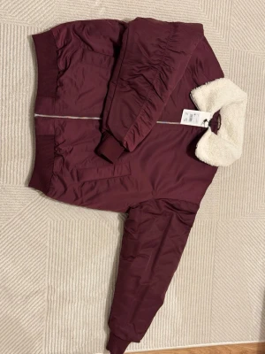 Vinröd bomberjacka med teddykrage - Säljer en vinröd bomberjacka med fluffig vit teddykrage. Jackan har ribbade muddar, två fickor och dragkedja framtill. Materialet är polyester och kragen är i mjuk teddy. Perfekt för dig som vill ha en chill och snygg look. Oversize storlek, passar även dig som har M.