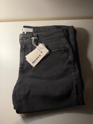Mörkgrå jeans från NA-KD - Jeans från NA-KD i modell ”jeans med låg midja”, färg ”mörkgrå”. Kolla på deras hemsida för att se hur de sitter på. Helt nya med prislapp kvar (nypris 699kr). Storlek 32,  men väldigt stora i storleken, sitter som 34.