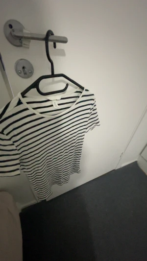 Randig t-shirt från H&M - Säljer en fräsch vit t-shirt med svarta horisontella ränder från H&M. T-shirten har rund hals och korta ärmar, perfekt för en chill och stilren look. Materialet är mjuk bomull som känns skönt mot huden.