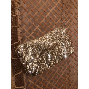 Glittrig guld axelväska med paljetter - Snygg axelväska i guld med glittriga paljetter över hela ytan och kedjeaxelrem. Väskan har en rektangulär form och stängs med dragkedja upptill. Insidan är fodrad i en varm gul ton. Perfekt för att lyfta din outfit med extra bling. Aldrig använd.