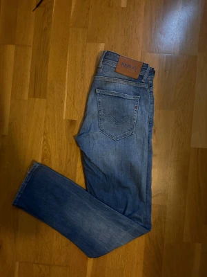 Replay jeans  - Säljer ett par Replay Grover jeans i straight fit med klassisk femficksdesign. Jeansen är blå med snyggt slitna detaljer och har en läderpatch med Replay-logga bak. Materialet är jeans och passformen är riktigt nice 