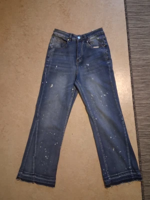Blå wide jeans från Fashion Jeans - Säljer ett par blå jeans från Fashion Jeans med coola färgstänk och råa, fransiga benslut. Modellen är wide fit med klassisk femficksdesign och normal midja. Perfekta för dig som vill ha en avslappnad och trendig look.