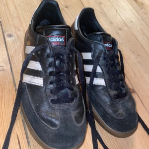 Adidas Samba svarta sneakers strl 37 ⅓ - Klassiska Adidas Samba sneakers i svart skinn med vita ränder och gummisula. Modellen har snörning och en låg profil, perfekt för dig som gillar retrostil. Ikonisk Adidas-logga på plösen. Dock en ända av det ena skosnöret har gått av. Men det gör inte mycket eftersom det är nästan samma längd som det andra snöret .Skorna är i fint skick. Inte använda mycket alls. Nypris 1300kr                                                         https://www.unisportstore.se/sneakers/adidas
