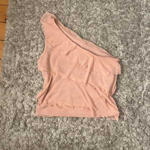 Ljusrosa mesh oneshoulder topp - Säljer en ljusrosa oneshoulder topp i mesh med volangdetaljer ifrån Cubus i strl XS, har klippt av lappen i ryggen eftersom den va väldigt obehaglig och kliade. Toppen har en asymmetrisk design och är ärmlös på ena sidan, vilket ger en unik och trendig look. Perfekt för dig som gillar romantiska och feminina plagg med lite edge. Suuuupersnygg men säljer pga att den inte kommer till användning nu under hösten tyvärr💞💞