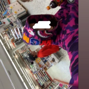 BAPE Shark Hoodie lila/rosa camo - Säljer en ikonisk BAPE Shark Hoodie med lila och rosa camouflage-mönster. Hoodien har dragkedja och huva. Den är använd ungefär 5ggr och säljer nu då jag vuxit ifrån stilen. Hoodien är äkta därför lite dyrare, köpt för 1000kr