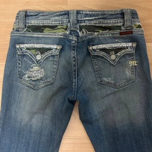 bootcut miss me jeans - snygga jeans från miss me med bootcut passform. slitna fickor med camouflage-tyg och paljettdetaljer. jeansen har låg midja och är i bra skick