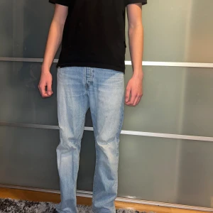 Levi's 501 ljusblå jeans straight fit - Midja 30 längd 32. Ljusblå klassiska Levi's 501 jeans med rak passform och normal midja. Jeansen har fem fickor, knappgylf och den ikoniska röda Levi's-taggen på bakfickan. Tillverkade i slitstarkt bomullsjeansmaterial, perfekt för en chill och avslappnad stil.