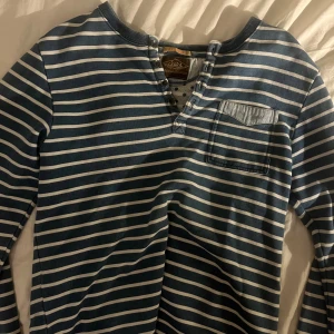 Randig långärmad tröja Scotch & Soda - Snygg långärmad tröja från Scotch & Soda i marinblått och vitt med horisontella ränder. Tröjan har knappslå vid halsen och en bröstficka. Tillverkad i mjuk bomull, perfekt för dig som gillar avslappnad stil med lite edge.